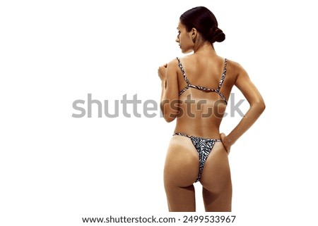 Woman stands in zebra-print bikini, showing off her deeply tanned skin and distinct tan lines against white studio background. Concept of beauty, body care, dermatology, summer season, protection.