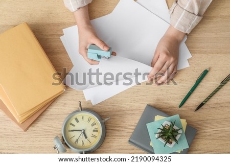 Woman with stapler, paper sheets, books and alarm clock at wooden table