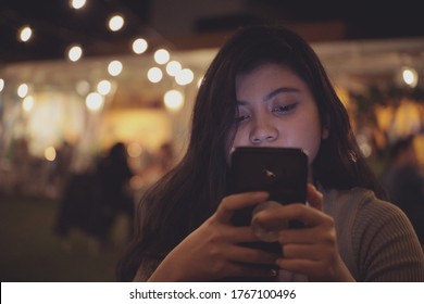 Woman Staring At Phone At Night With Blurry Crowd As Background. Woman Looking At Cellphone Screen At Night. Asian Women Staring At Smartphone At Night.