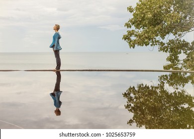 Woman staying on swimming pool with reflection on water. Sea and sky on background. Abstract portrait