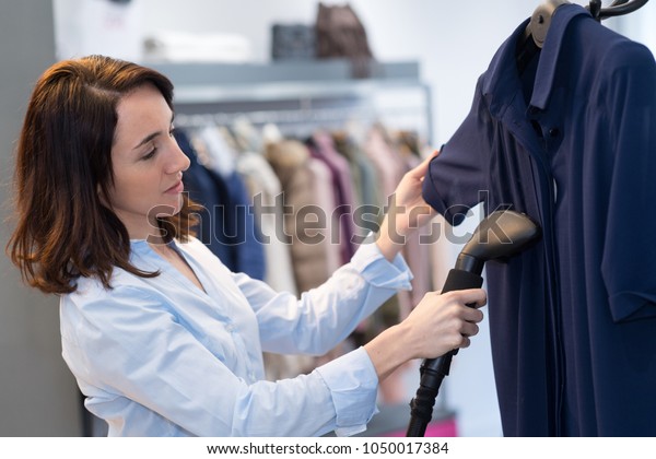 woman\
with steamer cleaning clothes in dry-cleaning\
salon