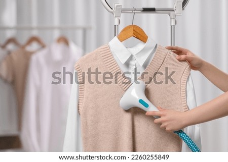 Woman steaming clothes on hanger at home, closeup
