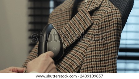 Woman steams plaid jacket with electric steamer at home. Dry cleaning clothes. Household and home equipment for housework.
