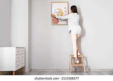 Woman With Stepladder Hanging Painting On Light Wall