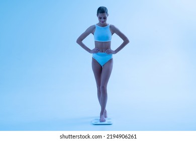 Woman Stepping On Weight Scales In Neon Light Dressed In Underwear, Happy With Results Of Strict Low Carb Diet And Intensive Workouts. Losing Weight, Keep Fit, Toned Body, Flat Stomach Concept