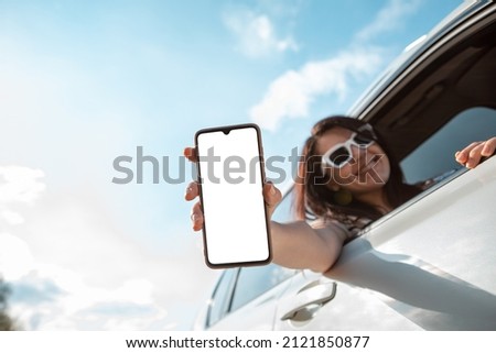 woman stick out of car window holding phone with white screen copy space rent app travel concept