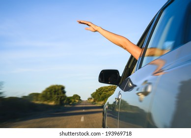 Woman Sticking Arm Out Of The Car Window On Roadtrip. Female Driver Hand Feeling The Air And Freedom.