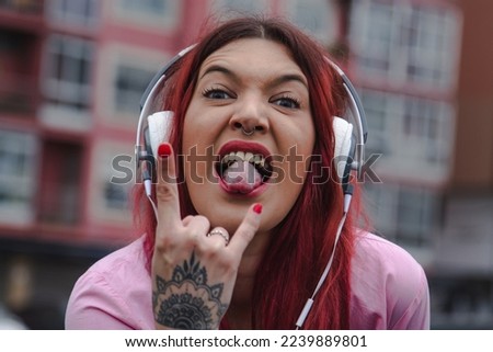 woman sticking out her tongue with rebel expression in the street with headphones