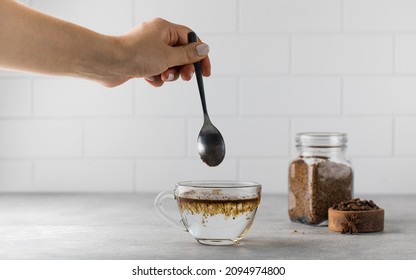 Woman stirs instant coffee in glass mug with boiled water on grey stone table - Powered by Shutterstock