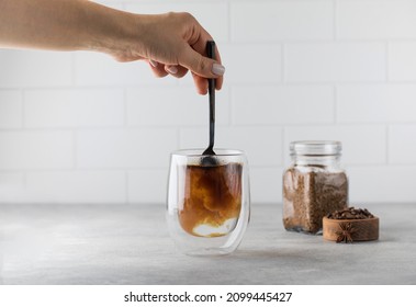 Woman stirs instant coffee in glass mug with boiled water on grey stone table - Shutterstock ID 2099445427
