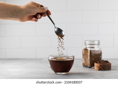 Woman stirs instant coffee in glass mug with boiled water on grey stone table - Shutterstock ID 2104180037