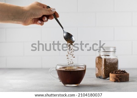Woman stirs instant coffee in glass mug with boiled water on grey stone table