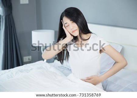 Woman stomach pain and headache on her bed in the bedroom