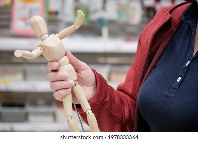 Woman In A Store Chooses To Buy A Figurine Of A Wooden Man. The Concept Of Hobbies, Creativity And Needlework. Hands Close Up Shot