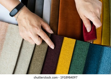 A woman in a store chooses a fabric for upholstered furniture in her new apartment, points to the color she liked in the catalog of special fabrics, close up. Top view
