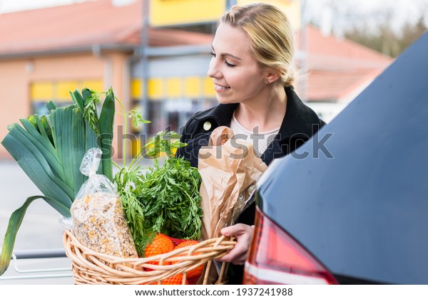 Woman storing basket with groceries into trunk\
after shopping