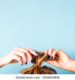 The Woman Straightens The Disheveled Bun On Her Head With Her Hands With A Black Manicure. Dark Hair Is Tied With A Transparent Spiral Elastic Band. Modern Fast Hairstyle. Blue Background. Copyspace