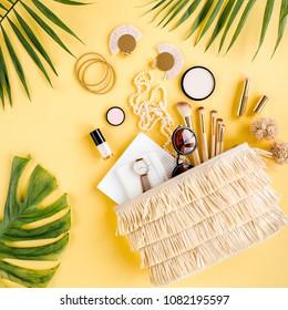 Woman Straw Bag With Travel Accessories, Makeup Brushes, Cosmetics, Golden Accessories And Tropical Palm Leaf On Yellow Background. Travel Concept Background. Top View. Flat Lay. 