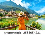 Woman with straw hat admiring the picturesque village of alleghe reflected on the lake in the italian dolomites during a sunny summer day