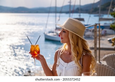 Woman in straw hat drinking aperol Spritz cocktail at summer cafe terrace