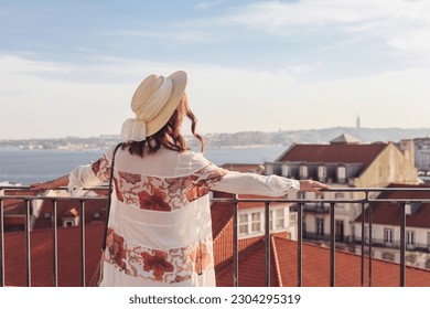 Woman in a straw hat looking over the rooftops of the Lisbon town 