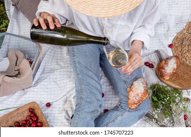 Woman in straw hat on picnic holding a glass of wine Top view. Aesthetic picnic outdoors with wine and berries and croissants.  - Powered by Shutterstock