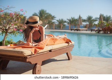 Woman in a straw hat relaxing on a daybed near a luxurious summer pool hotel Egypt, concept time to travel