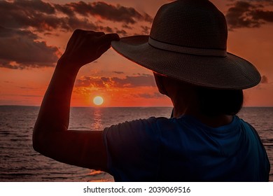 A woman with a straw hat  watching sunset on the beach