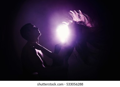  A woman with streaming hair sitting on a man's lap. Couple in contrast back light