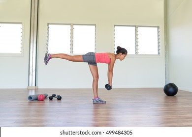 Woman strength training at gym exercising hamstring and lower back muscles with single-leg romanian deadlift exercises with free weights dumbbells. Asian girl alone indoors in fitness center room.