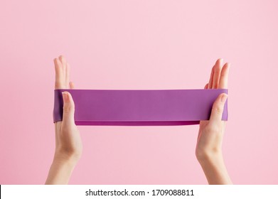 Woman stretch fitness band. Violet rubber for home exercises. Indoor and outdoor workout. Sport and healthy active lifestyle concept. Isolated on pink background