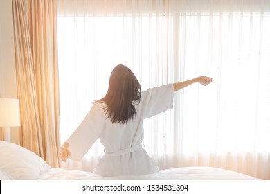 Woman stretching in bed after waking up, back view. Woman sitting near the big white window while stretching on bed after waking up with sunrise at morning, back view. - Shutterstock ID 1534531304