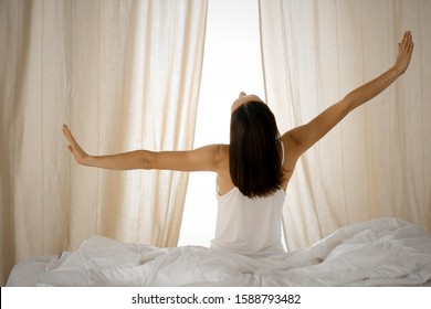 Woman stretching hands in bed after wake up, sun flare . Brunette entering a day happy and relaxed after good night sleep and back view. Concept of a new day and joyful weekend - Shutterstock ID 1588793482