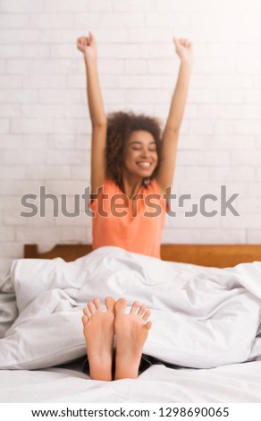 Woman stretching happily in bed after waking up, focus on feet