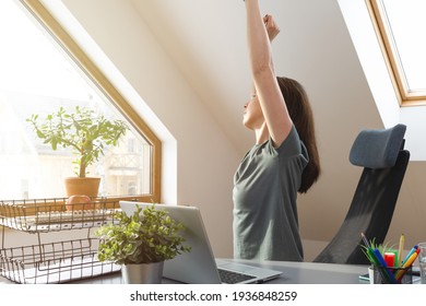 Woman Stretching Her Hands Up At Office Desk In A Break From Work At Home Office. Exercise And Healthy Living Concept.