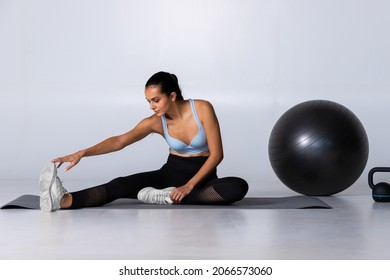 Woman Stretching Her Legs Touching Toes With Hands On Mat With Fitness Equipment On The Floor, Fit Female After Workout Cool Down Stretch