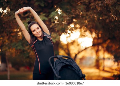 Woman Stretching in the Park Next to a Baby Stroller. Fitness mom ready for postnatal body recovery and exercising 
