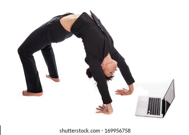 Woman stretching in yoga pose whilst working on a laptop. Isolated on white.