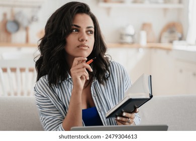 Woman in striped shirt thinking with pen and notebook, lounging with phone, adjusting sleep mask, sitting in the kitchen with rolling pin, celebrating while on a phone call - Powered by Shutterstock