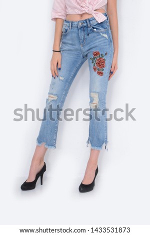 Woman in stripy shirt with embroidered flowers, pattern torn jeans and black high heels shoes posing
