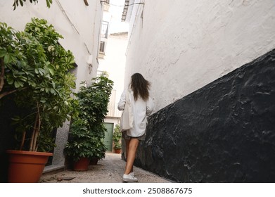 A woman strolls through a narrow alley in a European city, surrounded by lush potted plants, capturing a serene and adventurous spirit of urban exploration. - Powered by Shutterstock