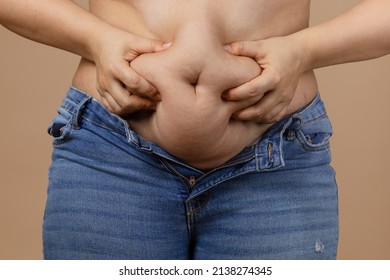Woman strongly squeezing flabby abdomen to show extra weight wearing unzipped jeans of blue color. Sudden weight gain. Visceral fat. Body positive. Tight little clothes. Need for wardrobe change.