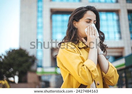 Woman struggling with allergy. Itchy eyes and sneezing. Attractive young adult woman coughing and sneezing outdoors. Sick people allergy or virus influenca concept.