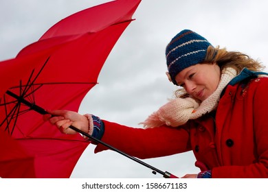 A Woman Struggling To Put Up An Umbrella In The Wind