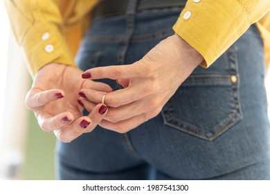 a woman in struggling to remove wedding ring from her finger holding hands behind his back. remove the ring from your finger. The concept of treason and betrayal. Divorce.