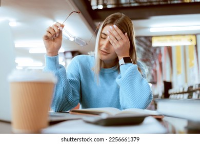 Woman student, tired with headache and university burnout, stress about paper deadline or study for exam in library. Campus, college studying fatigue with scholarship problem, pain and mental health - Powered by Shutterstock