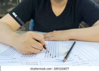 Woman students hand holding pencil writing selected choice on answer sheets and Mathematics question sheets. students testing doing examination. school exam