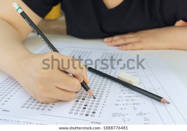 Woman students hand holding\
pencil writing selected choice on answer sheets and Mathematics\
question sheets. students testing doing examination. school\
exam