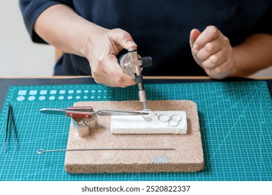 A woman in a studio works on jewelry using a gas torch to heat metal. Workplace of jeweler. - Powered by Shutterstock