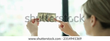 Woman studying watermarks on money dollars in front of window closeup